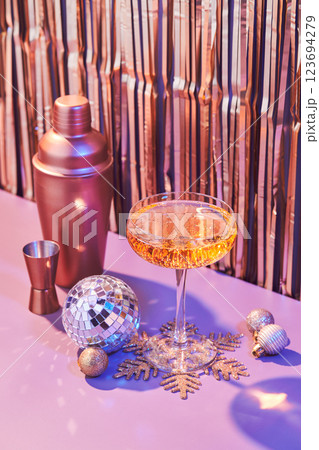 Splash in champagne glass, cocktail glass, shaker, and jigger on pink table with Christmas decorations 123694279