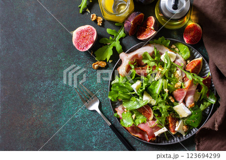 Healthy food concept. Autumn salad with figs, prosciutto, arugula, spinach, cheese, walnuts and honey on a stone countertop. Top view flat lay background. Copy space. 123694299