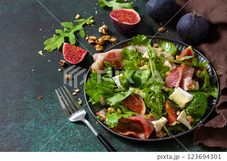 Healthy food concept. Autumn salad with figs, prosciutto, arugula, spinach, cheese, walnuts and honey on a stone countertop. Copy space. 123694301