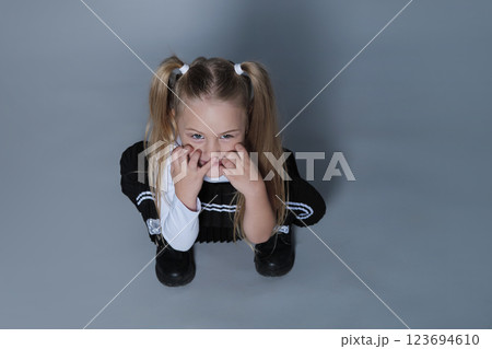 A young girl with pigtails crouches down playfully, making a funny face by scrunching her nose and pulling at her cheeks. Her mischievous expression captures a moment of childhood fun. A young girl with pigtails crouches down playfully, making a funny face by scrunching her nose and pulling at her cheeks. Her mischievous expression captures a moment of childhood fun. 123694610