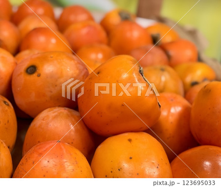 A pile of ripe juicy orange persimmons in a box, on sale at a supermarket vegetable stand, showcases organic, vegetarian and healthy food. Close-up 123695033