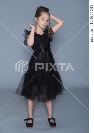 A girl in a black dress with tulle ruffles poses gracefully, showcasing the dress's intricate layers. The scene highlights sophistication in children's clothing, promoting timeless style and youthful A girl in a black dress with tulle ruffles poses gracefully, showcasing the dress's intricate layers. The scene highlights sophistication in children's clothing, promoting timeless style and youthful 123695242