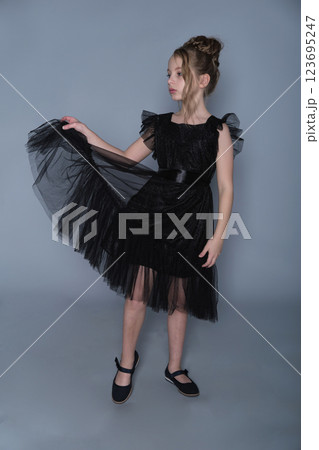 A girl stands gracefully in a black ruffled dress, lifting the fabric to reveal the delicate tulle layers. The photo emphasizes elegance and poise, highlighting modern trends in children's formal wear A girl stands gracefully in a black ruffled dress, lifting the fabric to reveal the delicate tulle layers. The photo emphasizes elegance and poise, highlighting modern trends in children's formal wear 123695247