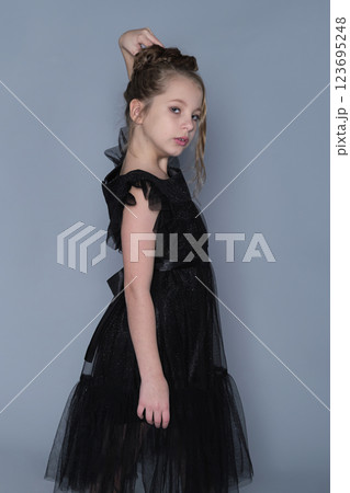 A young girl in a black ruffled dress poses playfully with her arms raised, showing a fun and lighthearted moment. This image captures the blend of elegance and youthful spirit in children's fashion. A young girl in a black ruffled dress poses playfully with her arms raised, showing a fun and lighthearted moment. This image captures the blend of elegance and youthful spirit in children's fashion. 123695248