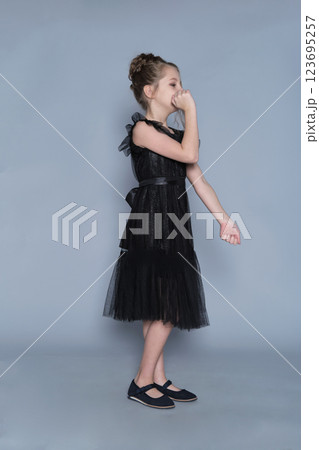 A young model in a flowing black dress poses with her arms extended, showing a playful and carefree attitude. This image reflects the balance between elegance and childhood fun in fashion photography. A young model in a flowing black dress poses with her arms extended, showing a playful and carefree attitude. This image reflects the balance between elegance and childhood fun in fashion photography. 123695257