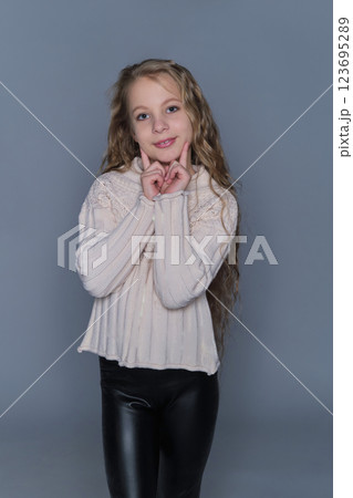 A young girl with long, wavy hair gently rests her hands on her cheeks, wearing a cozy knit sweater. This image emphasizes natural beauty and children's winter fashion, showcasing warmth and comfort. 123695289