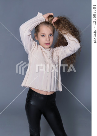A young girl poses with her hands in her hair, displaying the volume and texture of her natural curls. This image promotes the importance of children's hair care, focusing on nurturing and styling A young girl poses with her hands in her hair, displaying the volume and texture of her natural curls. This image promotes the importance of children's hair care, focusing on nurturing and styling 123695301