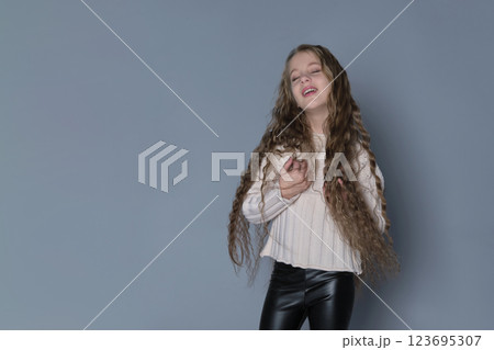 A young girl with long, flowing curly hair smiles as she runs her hands through her hair, enjoying the beauty of her natural locks. This image highlights the importance of natural hair care for A young girl with long, flowing curly hair smiles as she runs her hands through her hair, enjoying the beauty of her natural locks. This image highlights the importance of natural hair care for 123695307