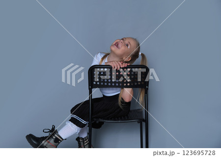 A playful 5-year-old girl is photographed in a studio, sitting on a black chair with a big, joyful expression. Dressed in a stylish one-shoulder top and black pleated skirt, she radiates energy and A playful 5-year-old girl is photographed in a studio, sitting on a black chair with a big, joyful expression. Dressed in a stylish one-shoulder top and black pleated skirt, she radiates energy and 123695728