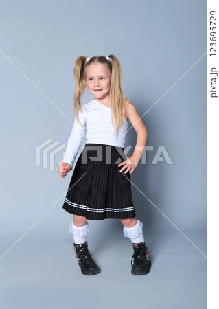 young girl showcases a chic look in a one-shoulder white top paired with a black pleated skirt and black boots. Her confident stance and playful expression bring out the modern trends in children's young girl showcases a chic look in a one-shoulder white top paired with a black pleated skirt and black boots. Her confident stance and playful expression bring out the modern trends in children's 123695729