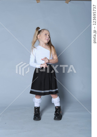 playful and confident little girl poses with her hand on her hip and a smile on her face. Dressed in a trendy one-shoulder top and black skirt, her personality shines through in this lively portrait 123695737
