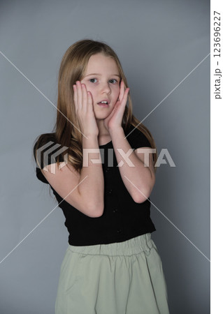 Girl with a look of amazement, her hands cup her cheeks. Emphasizes the innocence and curiosity inherent in youth. Girl with a look of amazement, her hands cup her cheeks. Emphasizes the innocence and curiosity inherent in youth. 123696227