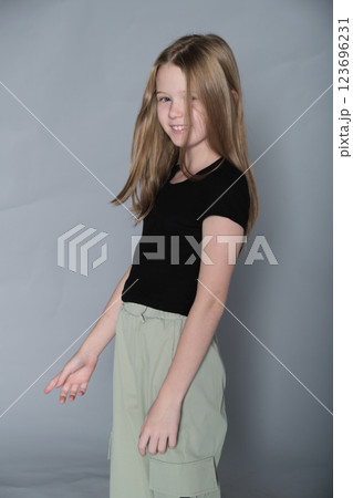 A young girl in a black top and green pants poses with her hand near her face, her expression calm and composed. This photo emphasizes the gentle and introspective nature of youth, captured in a A young girl in a black top and green pants poses with her hand near her face, her expression calm and composed. This photo emphasizes the gentle and introspective nature of youth, captured in a 123696231