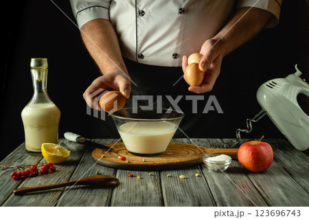 A skilled chef elegantly combines fresh eggs and milk in a glass bowl, surrounded by lemons and apples. European cuisine 123696743