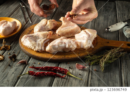 Seasoning chicken pieces with dried herbs and spices on a wooden board. The rustic kitchen features fresh ingredients and cooking tools for meal preparation Seasoning chicken pieces with dried herbs and spices on a wooden board. The rustic kitchen features fresh ingredients and cooking tools for meal preparation 123696749