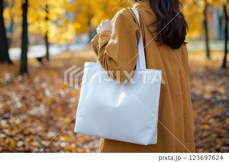 A woman is walking in a park with a white bag 123697624