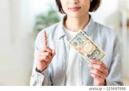 千円札を持って人差し指を立てるミドル女性 123697886