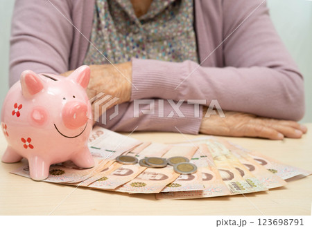 Retired elderly woman counting coins money with piggy bank and worry about monthly expenses and treatment fee payment. 123698791