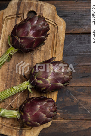 Whole purple raw roman artichokes on a dark wooden table top view. Fresh italian vegetables Whole purple raw roman artichokes on a dark wooden table top view. Fresh italian vegetables 123699458