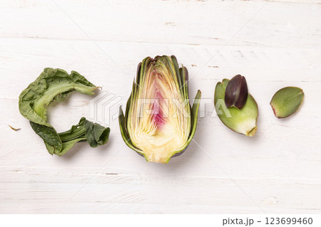 Half of purple raw roman artichokes on a white wooden table top view. Fresh italian vegetables 123699460