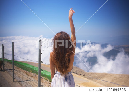 Woman standing on mountain peak above clouds enjoying the view Woman standing on mountain peak above clouds enjoying the view 123699868