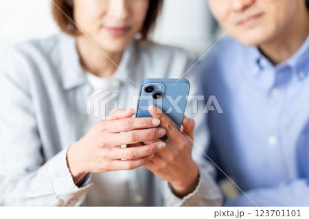 家でスマホを見ながら楽しそうに会話をするミドル夫婦 123701101