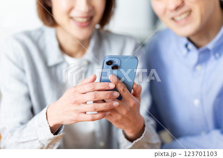 家でスマホを見ながら楽しそうに会話をするミドル夫婦 123701103