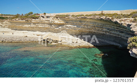 Stunning coastal landscape in Malta featuring layered limestone cliffs, secluded sandy cove, and crystal-clear turquoise waters under bright blue sky Stunning coastal landscape in Malta featuring layered limestone cliffs, secluded sandy cove, and crystal-clear turquoise waters under bright blue sky 123701357