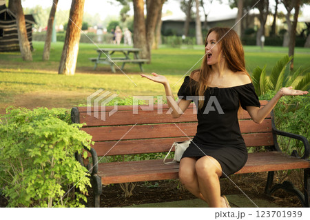 Surprised woman in black dress sitting on park bench with space for text Surprised woman in black dress sitting on park bench with space for text 123701939
