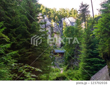 A rustic wooden cabin nestled by cliffs and surrounded by lush forest 123702016