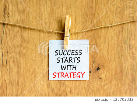 Success starts with strategy symbol. Concept words Success starts with strategy on beautiful white paper. Beautiful wooden background. Business and success starts with strategy concept. Copy space. Success starts with strategy symbol. Concept words Success starts with strategy on beautiful white paper. Beautiful wooden background. Business and success starts with strategy concept. Copy space. 123702332
