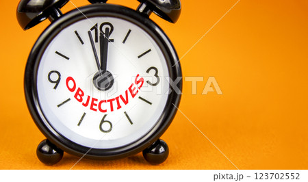 Objectives symbol. Concept word Objectives on beautiful orange paper. Beautiful orange paper background. Black alarm clock. Business objectives concept. Copy space. 123702552