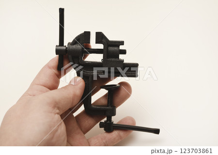 A small metal vise in his hand. The clamp. Tooling for locksmithing. A small metal vise in his hand. The clamp. Tooling for locksmithing. 123703861
