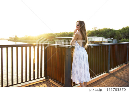 Woman in summer dress enjoying sunset view from wooden terrace Woman in summer dress enjoying sunset view from wooden terrace 123705870