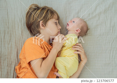 A young boy and his newborn brother lie together on a soft muslin blanket, sharing a tender sibling moment. A heartwarming scene of brotherly love, bonding, and the beginning of a lifelong connection 123706577