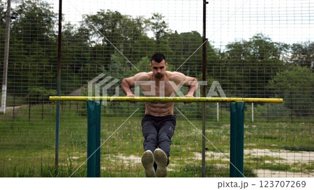 Hardy shirtless sportsman doing exercises on parallel bars at nature. Strong and muscular man working out at sports ground. Young athletic guy exercising outdoor. Concept of active healthy lifestyle 123707269