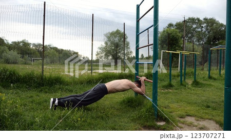 Young muscular athlete doing exercise on triceps at sport equipment outdoor. Male shirtless athlete working out at sport ground. Strong sporty man training at nature. Concept of healthy lifestyle Young muscular athlete doing exercise on triceps at sport equipment outdoor. Male shirtless athlete working out at sport ground. Strong sporty man training at nature. Concept of healthy lifestyle 123707271