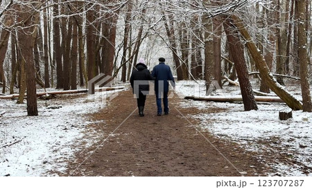 Mature couple going on snowy path at winter pine forest. Senior husband and wife walking through trail at coniferous woodland. Older pair of pensioners spending time together at nature 123707287