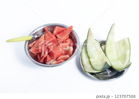 Closeup of watermelon with a spoon in bowls on a white background and watermelon rinds on a plate next to it. 123707508