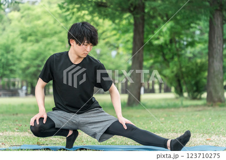 公園で運動前の準備運動・ウォーミングアップで屈伸するスポーツウェアの男性 123710275