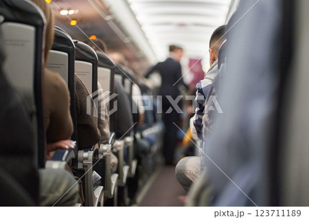 Along the passengers sitting on the seats on the plane. An unrecognizable flight attendant pours tea and serves hot drinks on board the plane. High quality photo Along the passengers sitting on the seats on the plane. An unrecognizable flight attendant pours tea and serves hot drinks on board the plane. High quality photo 123711189