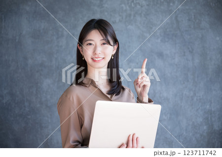 濃いグレーバックでパソコンを持つ女性　カメラ目線で笑顔でオススメ 123711742