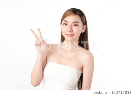 Beautiful young Asian woman with clean, fresh skin showing a two-finger gesture on a white background. Face care, beauty, and spa. Beautiful young Asian woman with clean, fresh skin showing a two-finger gesture on a white background. Face care, beauty, and spa. 123712052