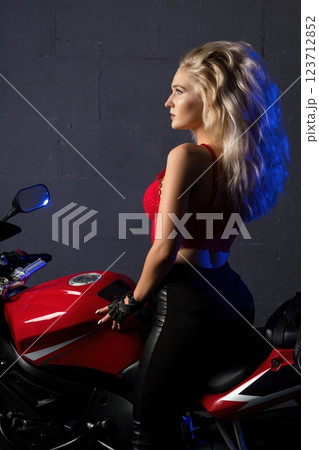 Woman poses confidently on a red motorcycle in a studio setting Woman poses confidently on a red motorcycle in a studio setting 123712852