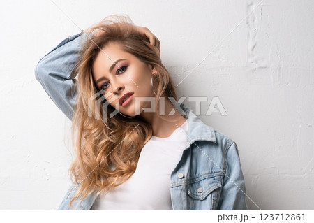 Young woman posing with long hair against a light wall wearing a denim jacket 123712861