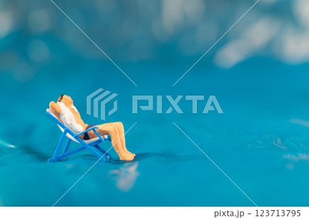 A man lounges on a beach chair, enjoying a peaceful moment on a textured blue surface resembling water A man lounges on a beach chair, enjoying a peaceful moment on a textured blue surface resembling water 123713795