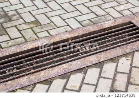 A rusty metal grate is currently sitting on a weathered brick sidewalk A rusty metal grate is currently sitting on a weathered brick sidewalk 123714639