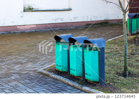 Three green trash cans are neatly lined up in front of a building Three green trash cans are neatly lined up in front of a building 123714645