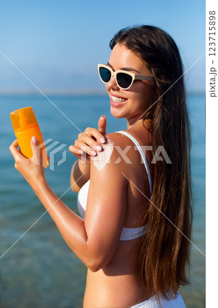 Applying Sun Cream on a Sunny Summer Day at the Beach With Radiant Blue Water in the Background Applying Sun Cream on a Sunny Summer Day at the Beach With Radiant Blue Water in the Background 123715898