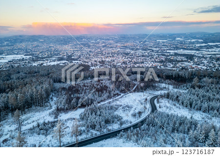 A serene winter evening unfolds above Liberec City, showcasing the enchanting snow-covered landscape with winding roads and vibrant pink hues in the sky. 123716187